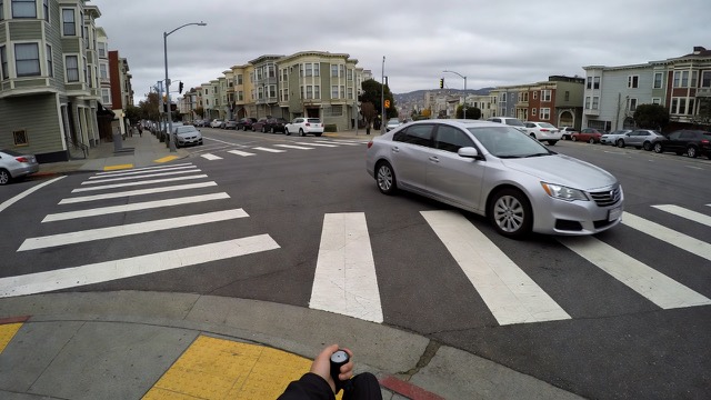 Grok Imagine scene: a silver sedan turning right into a crosswalk, seen from the curb
